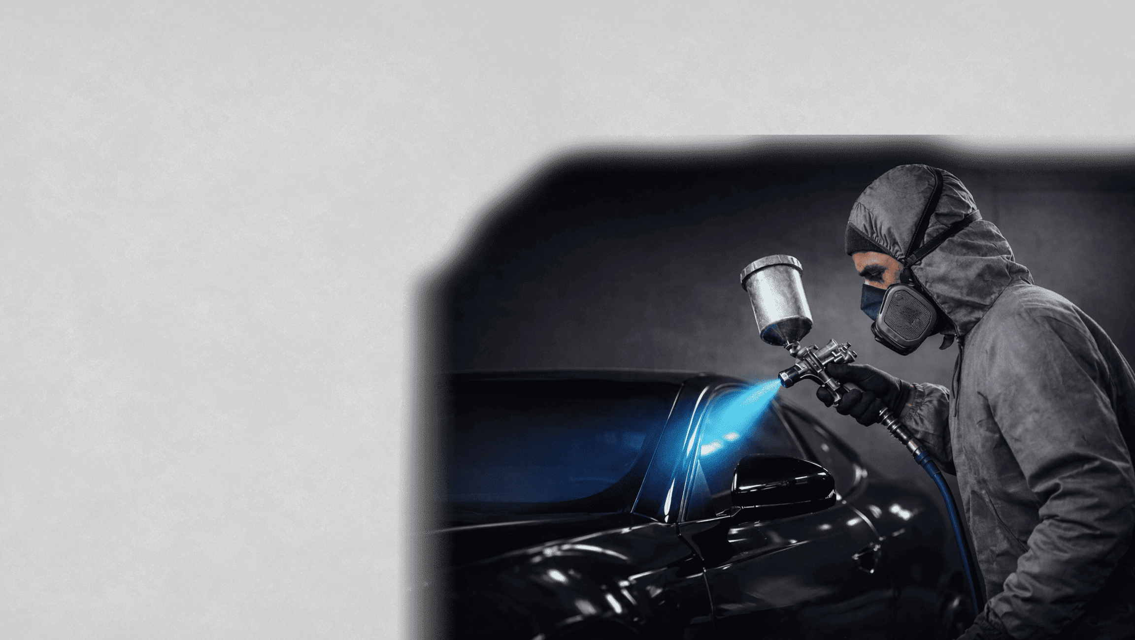 Fahrzeuglackierer sprüht mit einer Lackierpistole Lack auf ein Auto